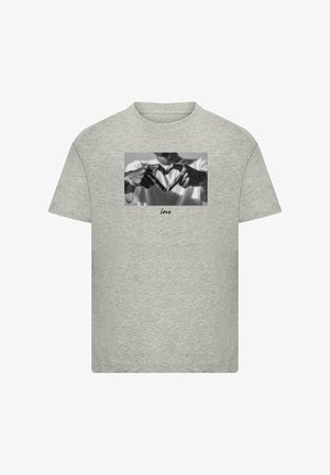 Világosszürke pamut póló, fekete-fehér grafikával, amely két kezet ábrázol, amint szív alakot formálnak, a kép alatt pedig a "Szeretet" felirat olvasható.