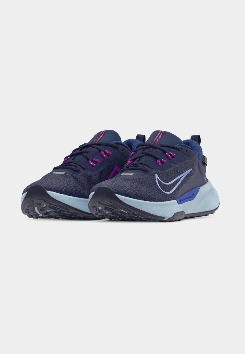 Par de zapatillas de running azul marino con suelas azul claro, ojales morados para los cordones y un swoosh blanco de Nike sobre un fondo liso.