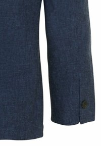 Manche en tissu texturé bleu foncé avec un petit bouton noir près du poignet, montrant une partie d'un vêtement.