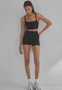 Sort crop top og højtsiddende shorts lavet af strækbart stof. Har tynde stropper og en tætsiddende design, parret med lyse sneakers.