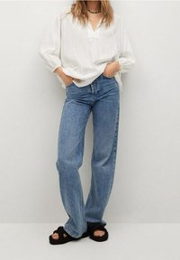 White, long-sleeve, V-neck shirt with a textured pattern; paired with high-waisted, wide-leg blue jeans and black woven sandals.