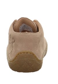 Beige Wildlederschuh mit abgerundetem Absatz, strukturiertem Sohlenboden und einem dezenten Muster. Das Innenetikett ist sichtbar. Die gummierte Basis sorgt für Halt.