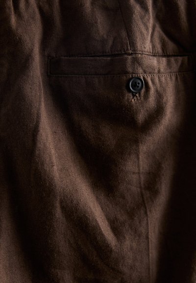 Bruine stoffen shirt met een subtiele textuur, een klein zakje en een zwart knoopdetail bij de halslijn.