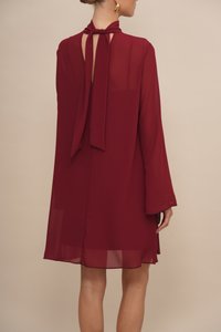 Bordeaux chiffon jurk met lange mouwen, een keyhole rug en een strik detail bij de hals. Licht en vloeiend, met een transparante afwerking.