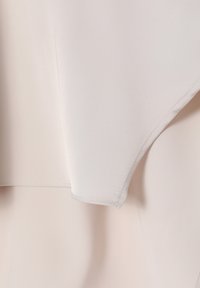 Gros plan d'un coin de tissu beige pâle avec des coutures détaillées et une texture lisse, montrant un design plié en couches.