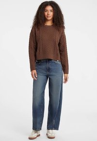 Brun kabelstrikket cropped sweater kombineret med mørkeblå, højtaljede denimjeans. Hvide sneakers med brune detaljer fuldender outfittet.