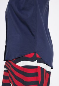 Camicia blu navy con orlo curvo indossata sopra una gonna multicolore con ampie strisce rosse, nere e bianche. Tessuto morbido, design casual.