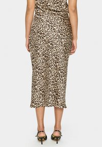 Jupe midi en imprimé léopard en tissu lisse, avec une taille ajustée et un ourlet évasé, présentant un léger éclat et des chaussures à talons élégantes.