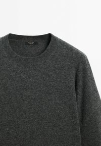 Pull en maille gris foncé avec un col rond. Texture douce avec une variation minimale du motif. Étiquette visible à l'intérieur du col.