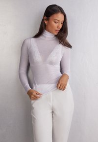 Transparent vit långärmad topp med en mock neck, prydd med en delikat spetsdesign vid halsringningen, kombinerad med vita skräddarsydda byxor.
