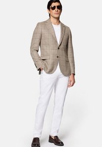 Beżowa marynarka w kratę z ciemnymi liniami, biała koszulka, białe spodnie, brązowe mokasyny i okulary przeciwsłoneczne. Dopasowany krój i zorganizowany design.