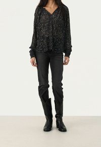 Blusa nera a maniche lunghe con motivo a pois dorati, scollatura a V e polsini arricciati, abbinata a jeans neri e stivali neri al ginocchio.