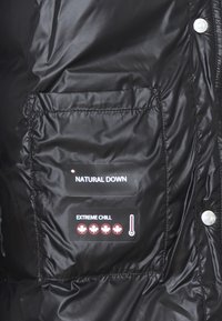 Giacca a vento nera con una finitura lucida, dotata di una tasca che mostra grafiche e icone "NATURAL DOWN" e "EXTREME CHILL".