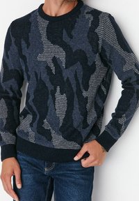 Marinblå crewneck-tröja med ett texturerat kamouflage-mönster i olika nyanser av blått och grått, med ribbade muddar och nederkant.