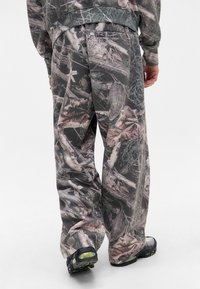 Camo-mønstrede afslappede bukser lavet af blødt stof, med jordnære nuancer af grøn, brun og grå, brede ben og elastisk talje.