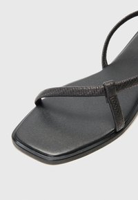 Zwarte platte sandalen met een gestructureerd bandontwerp, vierkante neus en een gladde zool. De banden zijn dun met subtiele details.