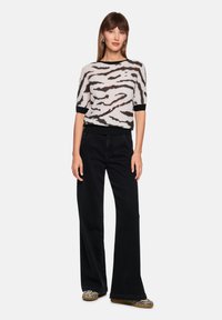 Hellgrauer Pullover mit schwarzem Zebramuster, kurzen Ärmeln und schwarzem, geripptem Saum, kombiniert mit hoch taillierten schwarzen Jeans mit weitem Bein.