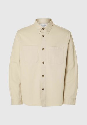 Camisa de botones de manga larga color beige con dos bolsillos en el pecho y botones marrones, exhibida sobre un fondo liso.