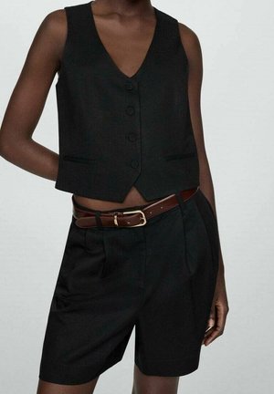 Gilet sans manches noir avec un col en V, cinq boutons et poches avant, associé à un short noir ajusté et une ceinture marron.