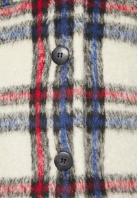 Tähtipaita villakangas, jossa on punainen, sininen, musta ja valkoinen väri pehmeällä pinnalla; sisältää mustan napin yksityiskohdan.