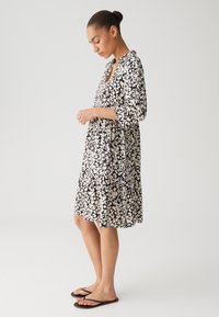 Black and beige patterned dress with three-quarter sleeves, tiered design, and a collar. Paired with black flip-flops.
