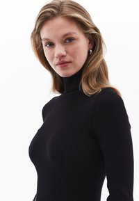 Schwarzer gerippter Rollkragenpullover mit langen Ärmeln, der eine enganliegende Silhouette und ein strukturiertes Gewebe für zusätzliche Details aufweist.