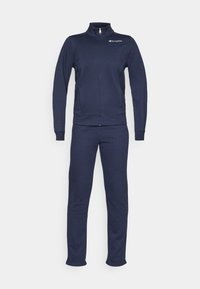 Ensemble de survêtement zippé bleu marine avec manches longues, poignets élastiques, poches latérales et logo Champion sur la poitrine gauche.
