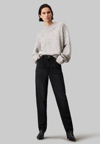 Suéter texturizado gris claro con cuello redondo y hombros caídos, combinado con jeans negros de cintura alta y botas negras de tacón puntiagudo.