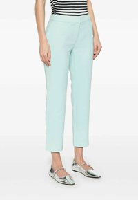 Pantaloni azzurri chiari, aderenti con una texture liscia, dotati di tasche frontali e gamba a lunghezza accorciata. Abbinati a scarpe piatte in argento lucido.
