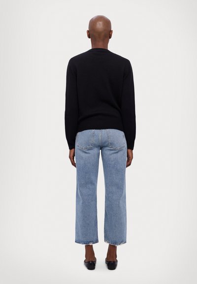 Zwart gebreid trui met een ronde hals, gecombineerd met lichtblauwe denim, wijde jeans met rauwe zomen en subtiele achterzakken.