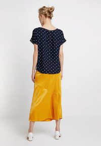 Námořnická halenka s puntíky a krátkými rukávy zkombinovaná s lesklou žlutou sukní po kolena s texturovaným vzorem a asymetrickým střihem.