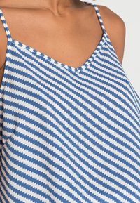 Blå och vit ärmlös topp med ett zigzag-mönster, V-halsringning och tunna band av mjukt tyg.