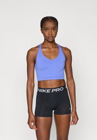 Ανοιχτό μοβ αθλητικό σουτιέν με λογότυπο Nike, σε συνδυασμό με μαύρο σορτς με ζώνη μέσης Nike Pro. Ομαλό, ελαστικό ύφασμα, μινιμαλιστικός σχεδιασμός.