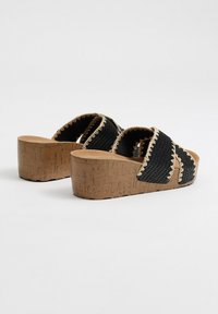 Sandalias de plataforma tejidas en negro con plantilla de corcho y detalles trenzados a lo largo de los bordes, con un diseño de tiras cruzadas.
