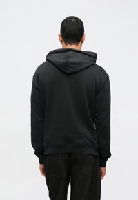 Sweatshirt preta com capuz espaçoso e punhos canelados, feita de tecido macio. A vista trasera mostra um ajuste descontraído e sem gráficos identificáveis.