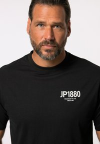 Schwarzes T-Shirt mit kurzen Ärmeln und Rundhalsausschnitt. Mit einem weißen Logo "JP1880" auf der Brust bedruckt. Weiches Baumwollmaterial, lässige Passform.