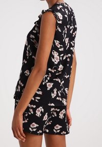 Blusa nera con maniche corte a volant, caratterizzata da motivi floreali rosa e crema, abbinata a pantaloni corti coordinati. Tessuto morbido al tatto.