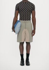 Olivgröna shorts med en beige panel, parat med en svart skjorta med ett mönster av halvmånar. Håller i en vikt blå denim.