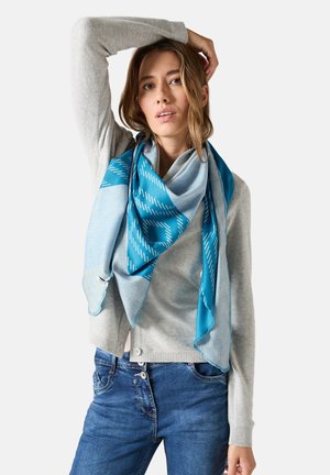 Blaue und hellblaue gemusterte Seidenschal, der über einem grauen Pullover getragen wird, mit dreieckiger Form und glatter Textur.