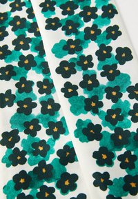 Floral fabric featuring various shades of green flowers with black outlines and golden centers on a white background, textured weave.
