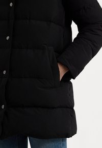 Černá zateplená bunda s prošívaným vzorem, se zapínáním na kovové druky a bočními kapsami. Bunda má uvolněný střih a měkký materiál.