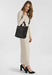 Sac en cuir texturé noir avec double anses et bandoulière réglable, agrémenté de détails en métal argenté, associé à une robe de couleur neutre.