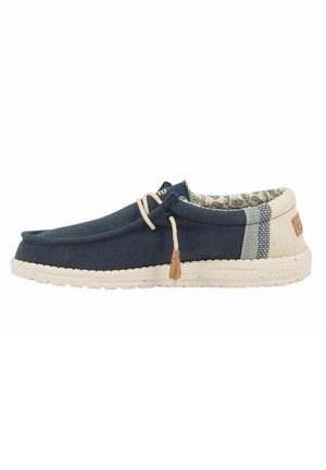 Scarpa slip-on in tela blu marina con accenti beige, cuciture texture e fodera interna a motivo. Presenta una suola leggera e lacci decorativi.