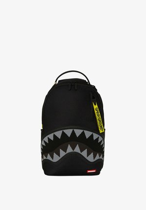 Zaino nero con un design a bocca di squalo grigio e nero, dotato di una tracolla con logo giallo e chiusura con doppizia. Finitura in tessuto liscio.