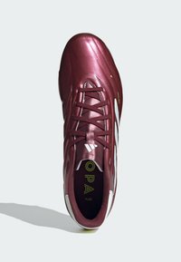 Zapato de fútbol burdeos con una superficie sintética brillante, diseño de cordones, acentos blancos y logo visible en la plantilla.