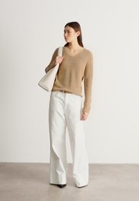 Beige strikket genser med V-hals, kombinert med hvite bukser med vide ben og svarte hæler. Bærer en strukturert hvit håndveske.