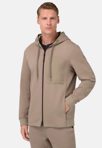 Beige mikina na zips vyrobená z mäkkej tkaniny, so kontrastnou náprsnou vreckom, kapucňou so šnúrkou a bočnými vreckami s rebrovanými manžetami.