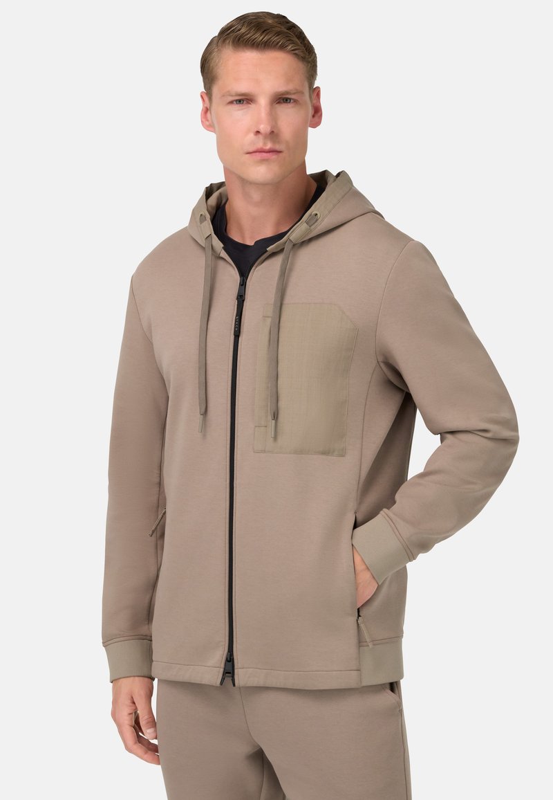Beige mikina na zips vyrobená z mäkkej tkaniny, so kontrastnou náprsnou vreckom, kapucňou so šnúrkou a bočnými vreckami s rebrovanými manžetami.
