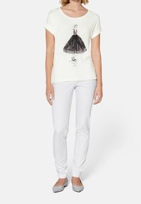 Camiseta blanca con una ilustración negra de una figura en un vestido, combinada con pantalones blancos ajustados y zapatos planos grises. Tejido suave.