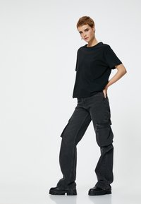 T-shirt nera a collo rotondo abbinata a pantaloni cargo grigio scuro. I pantaloni presentano tasche laterali e una vestibilità ampia. Scarpe con tacco nere completano il look.